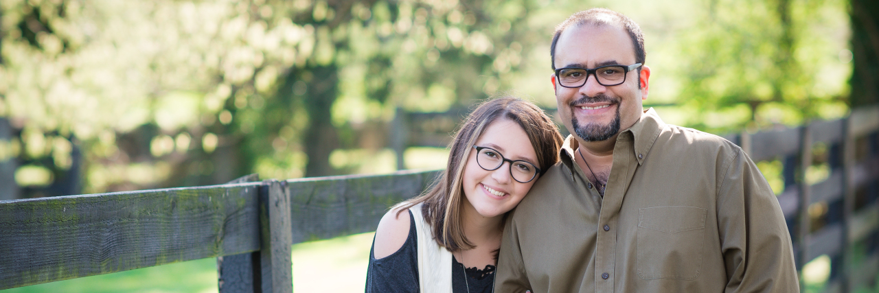Tips for Parenting With Chronic Pain and Fibromyalgia leonardo ramirez and his teenage daughter standing outside in front of a wooden fence and smiling.
