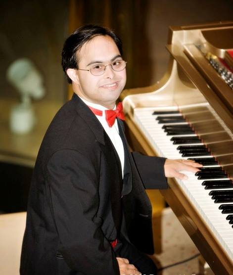 Sujeet Desai wearing a tuxedo and sitting at the piano, smiling at camera