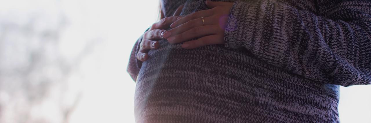 An image of a pregnant person's stomach with the sunlight in the background.