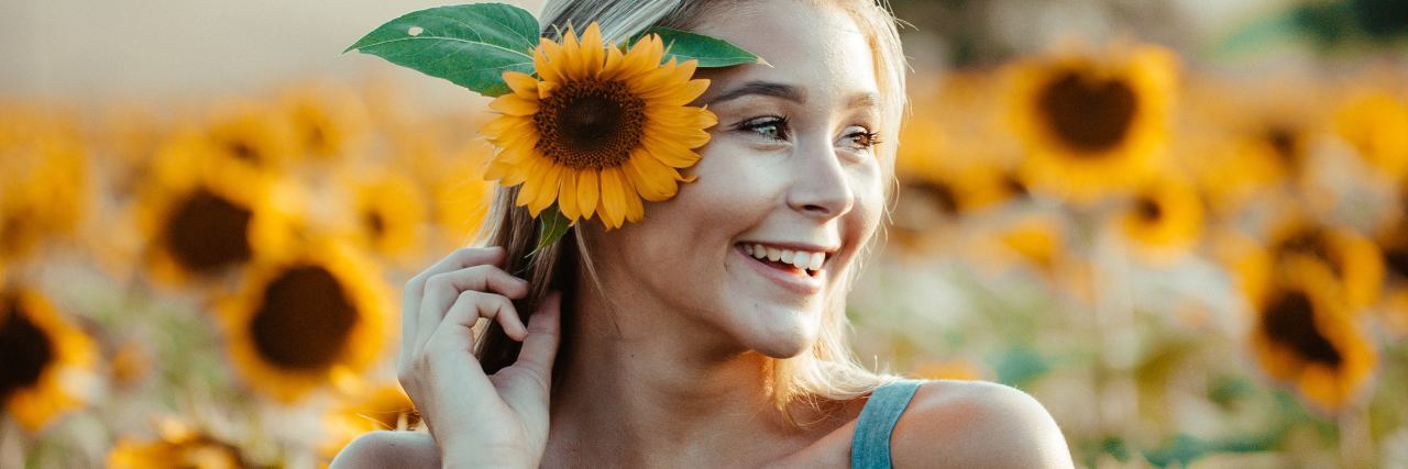 blonde woman in field of sunflowers smiling and holding one to the side of her hair
