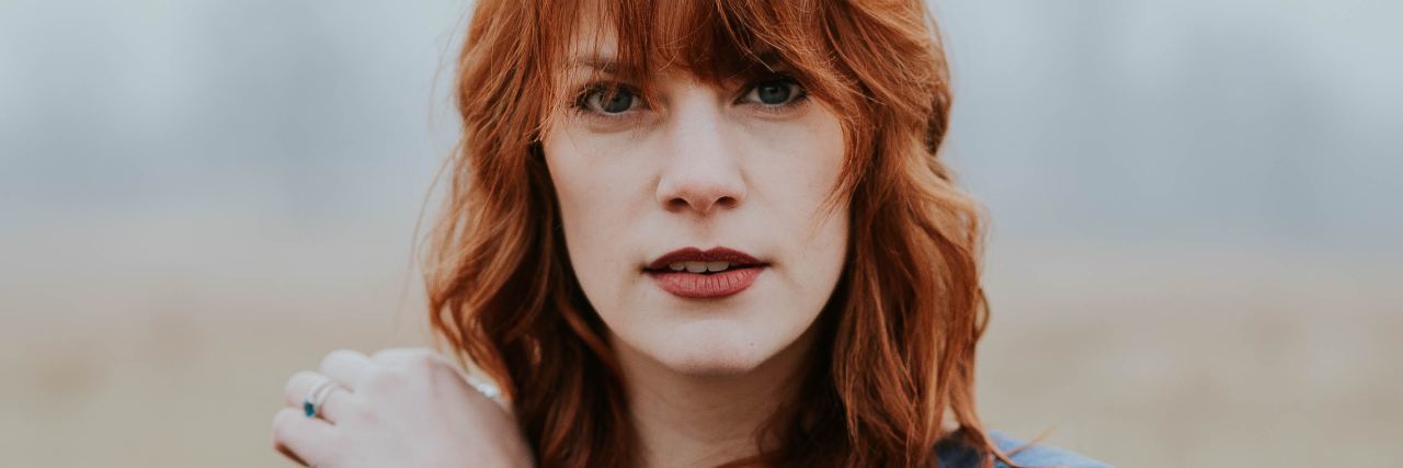 Read This If You're Asking If Therapy Is Worth the Financial Cost redhead woman looking into camera covering herself with her arms