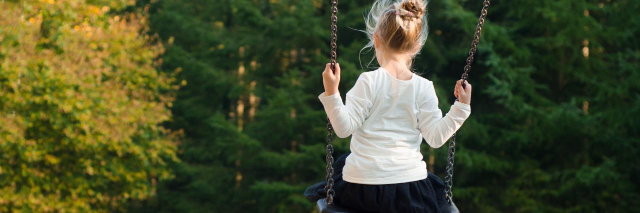 little girl alone on swing near trees