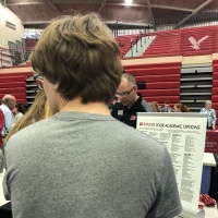 Back of tall teen at a college fair waiting to talk to a college representative
