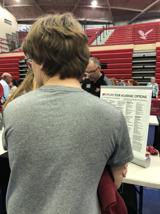 Back of tall teen at a college fair waiting to talk to a college representative