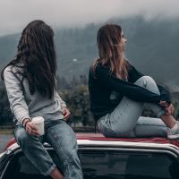 two young women sitting on roof of car by mountains
