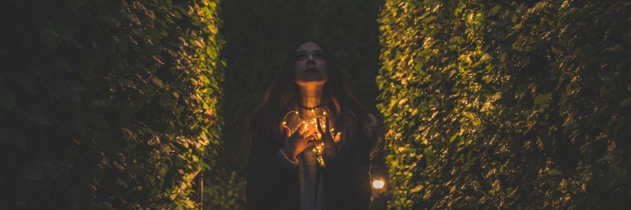 Do Highly Sensitive People Have Good Intuition? Woman standing between two hedges looking up while holding fairy lights