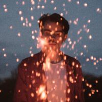 man standing in front of sparks from fire at night