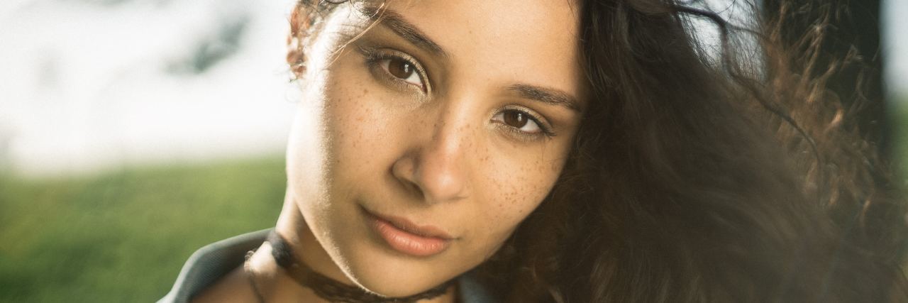 Being Shamed for Developing Chronic Illness Due to an Eating Disorder woman with long, curly hair standing outside and looking at the camera