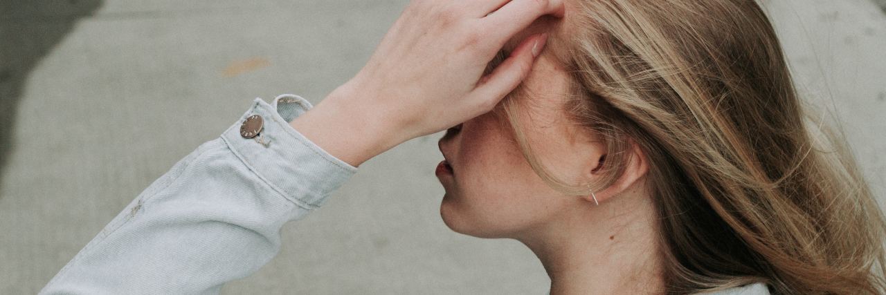 Requests People With Ehlers-Danlos Make to Help Manage Symptoms woman wearing a collared shirt and holding her head with her hand, blocking her face from view