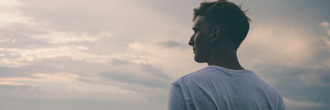 Learning How to Live, Add Value to the World With Multiple Sclerosis man wearing a white shirt and standing on a mountain, looking out over a valley