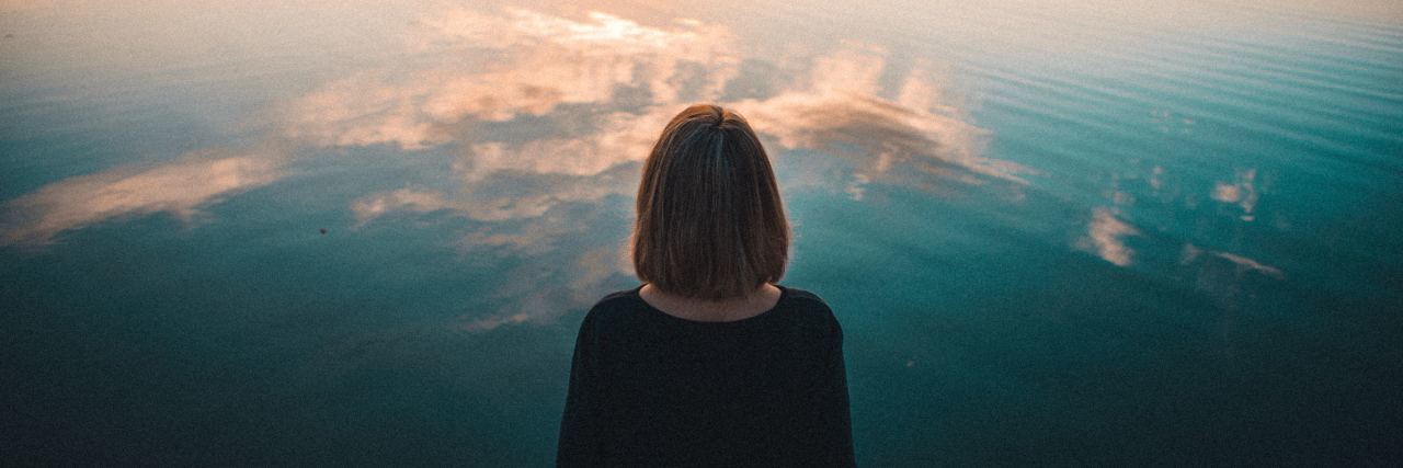 Losing Memories After Electroconvulsive Therapy woman facing still lake at sunset with trees and clouds reflected in water