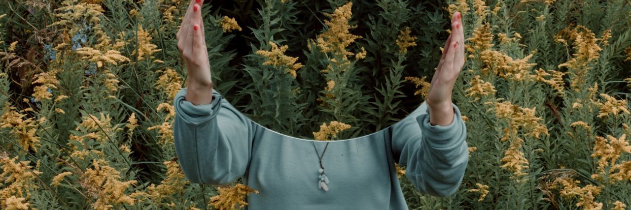 Woman standing with mirror hiding face in field of yellow flowers