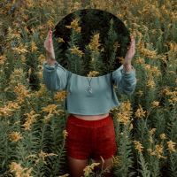 Woman standing with mirror hiding face in field of yellow flowers