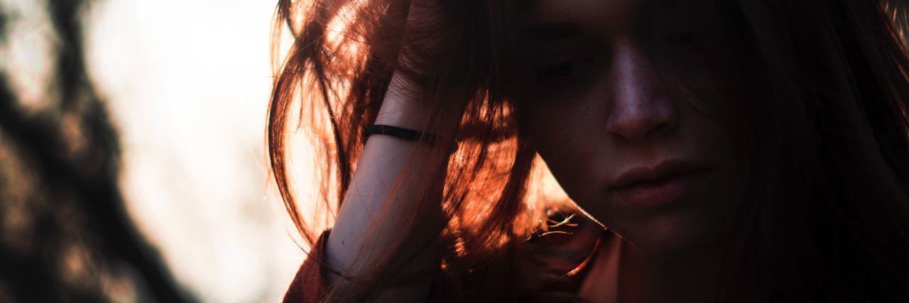 Things You Shouldn't Assume About My Anxiety close up of woman looking down with hand in hair backlit by sun