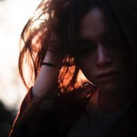 close up of woman looking down with hand in hair backlit by sun