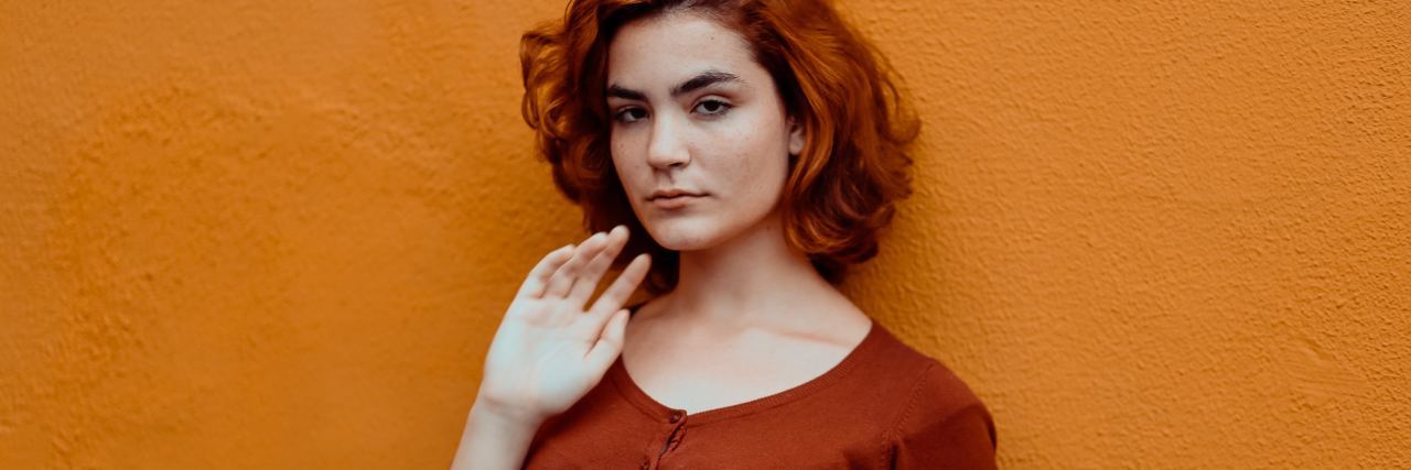 woman with red shirt and red hair standing against an orange wall