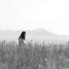 black and white photo of woman standing in field with long grass