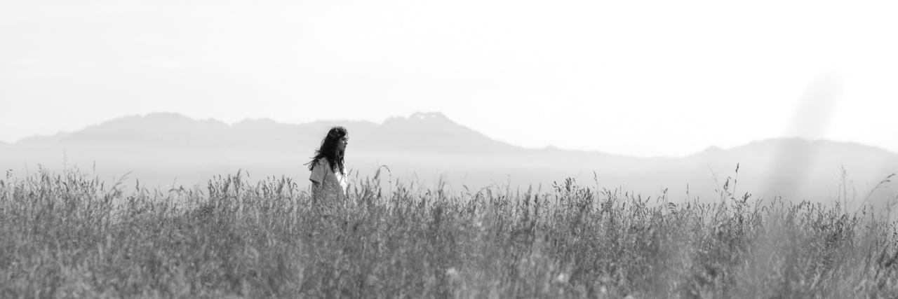 black and white photo of woman standing in field with long grass