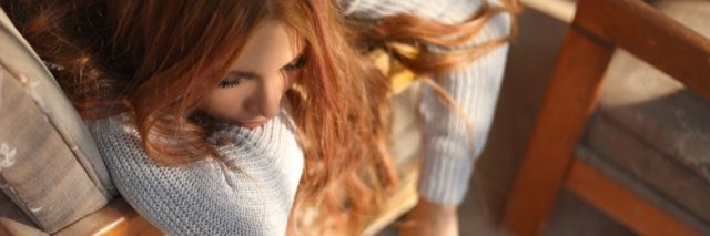 photo of redhead woman lying on sofa bathed in light looking bored or tired