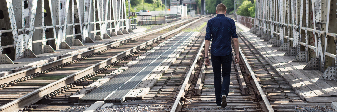 man walking away down train tracks with head bowed