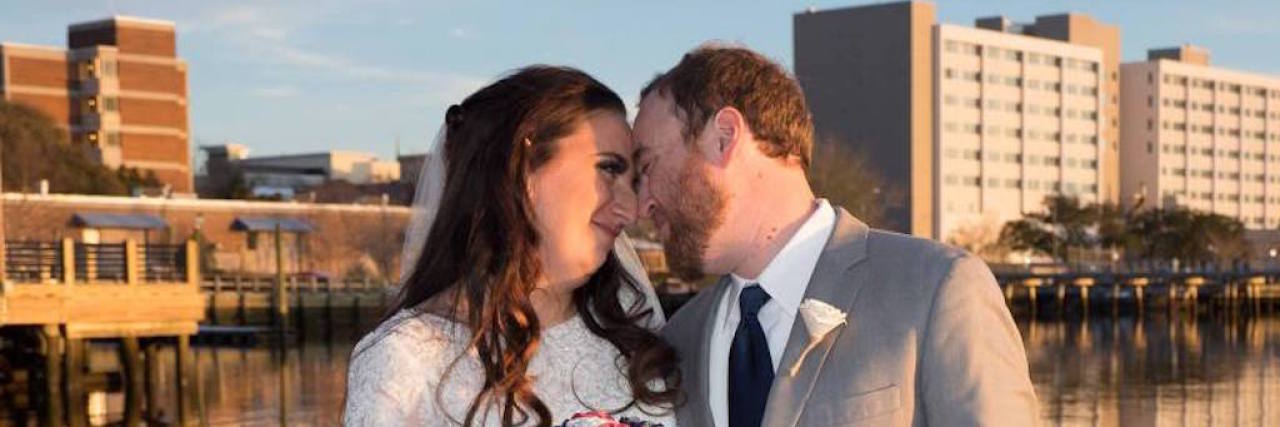 What It's Like Being Sick on Your Wedding Day the author and her husband posing in front of a lake and city on their wedding day