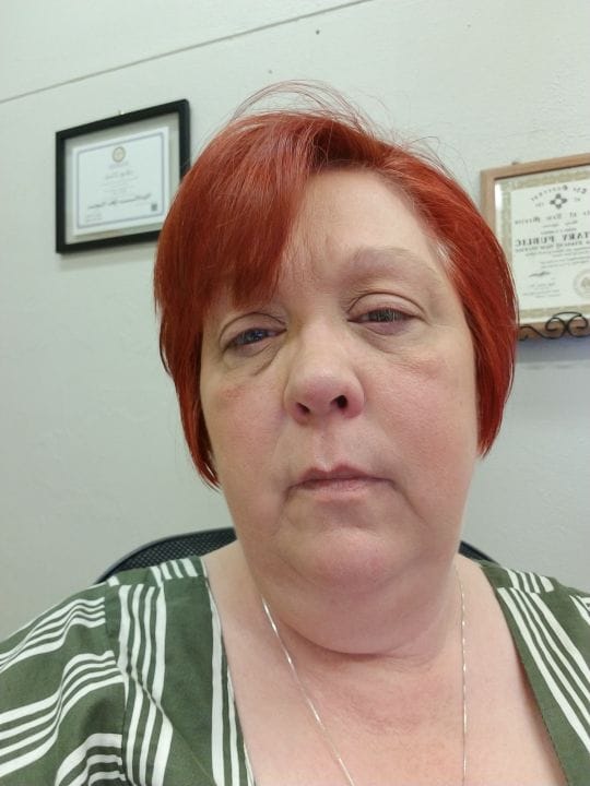 woman with red hair and a green shirt taking a selfie at work