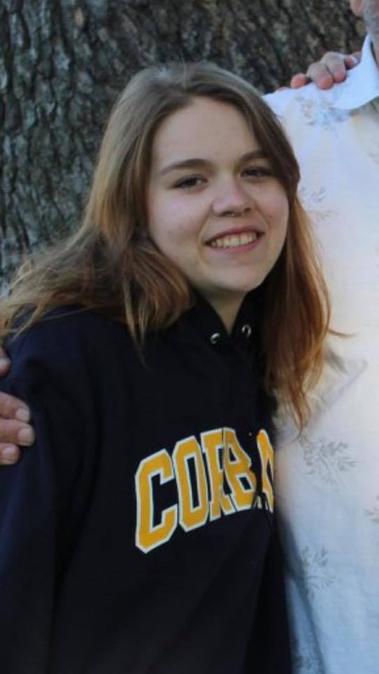 young woman wearing a sweatshirt and standing outside hugging someone in front of a tree
