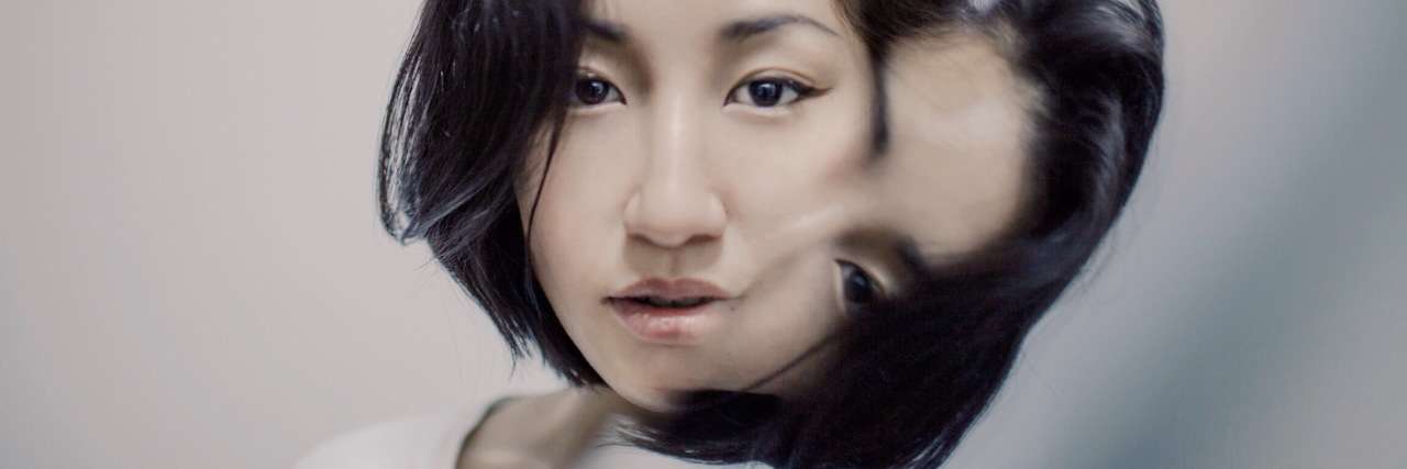 photo of asian woman looking into camera with mirror partly reflecting her face