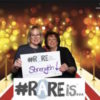 Betty and her friend holding a sign saying "rare is strength"