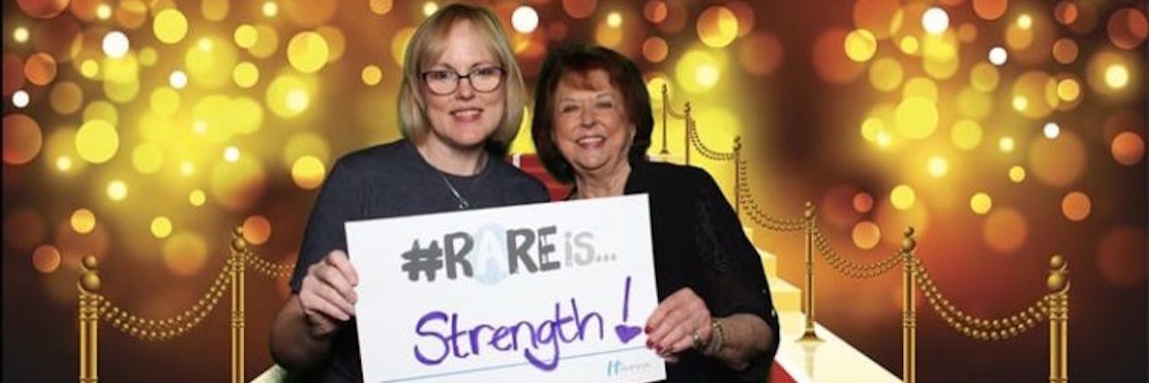 Betty and her friend holding a sign saying "rare is strength"