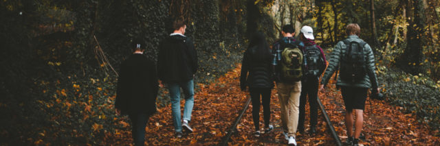 group of friends walking along train tracks in fall with backs to camera
