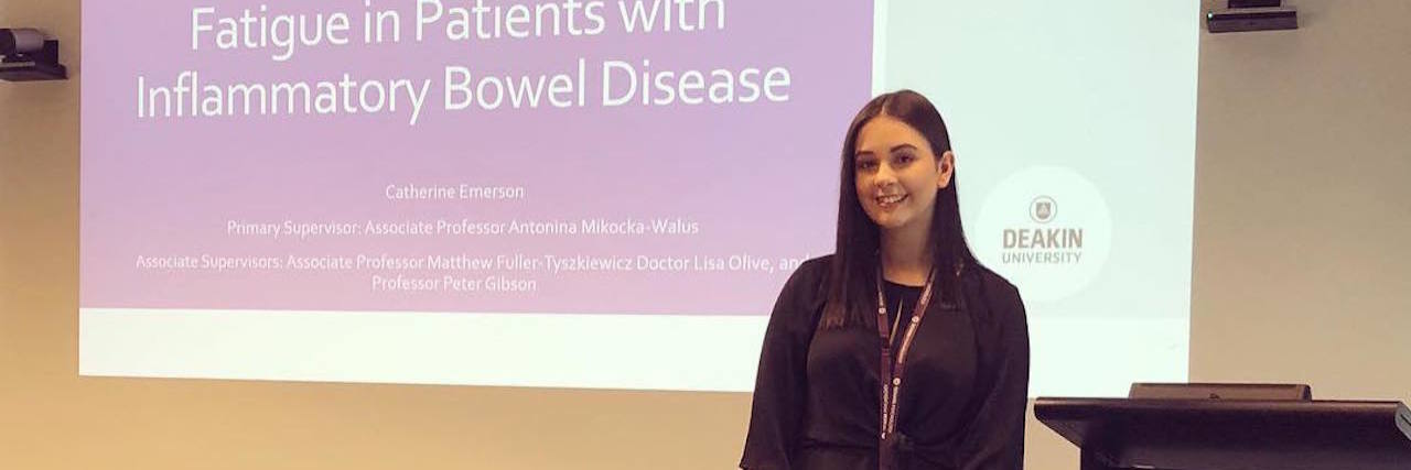 How My Crohn's Disease Diagnosis Helped Me Find My Purpose the author standing in front of a presentation at her PhD hearing