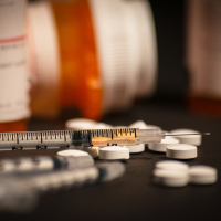 An injectable drug is loaded into a syringe while prescription medication is strewn about haphazardly.