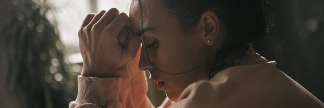 woman holding her hands together to her forehead looking sad