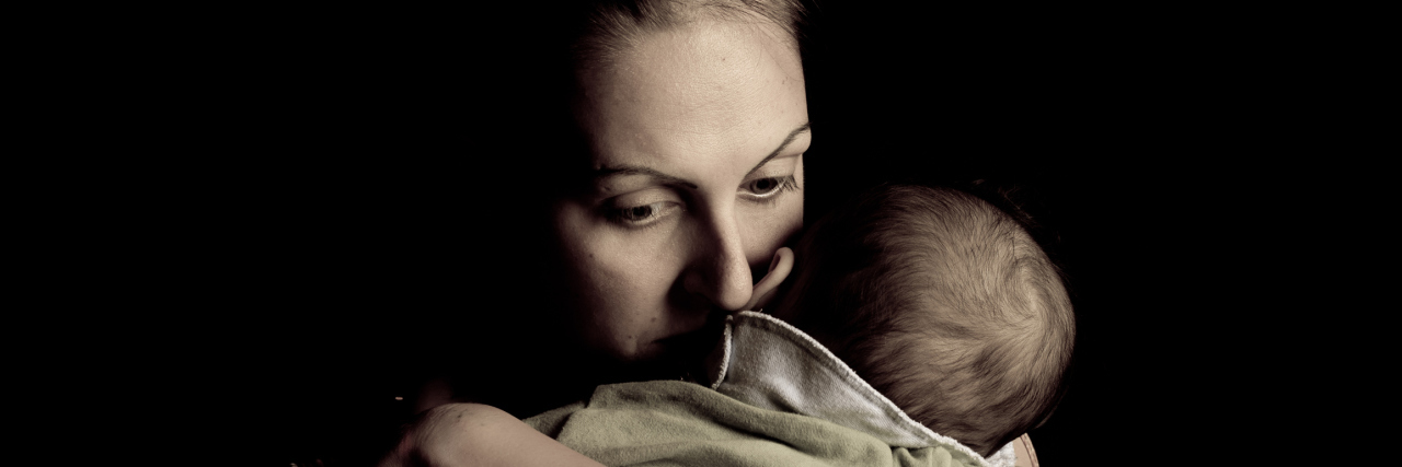 The Parenting Experience of Raising Kids With Disabilities Image of mother hugging her baby close, half her face buried on her baby's neck. Her expression shows love and concern.