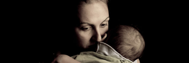 Image of mother hugging her baby close, half her face buried on her baby's neck. Her expression shows love and concern.