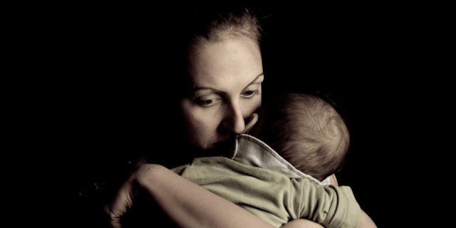 Image of mother hugging her baby close, half her face buried on her baby's neck. Her expression shows love and concern.