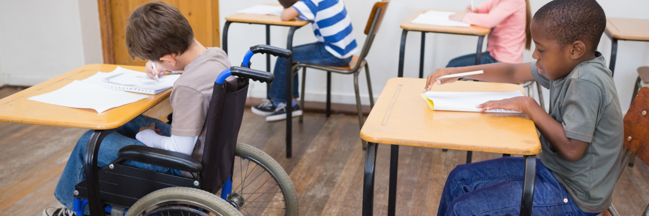 Disabled student writing at desk in classroom.