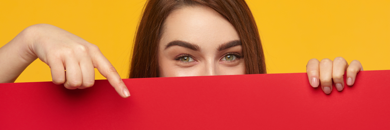 Model holding a colored piece of paper near her face, smiling