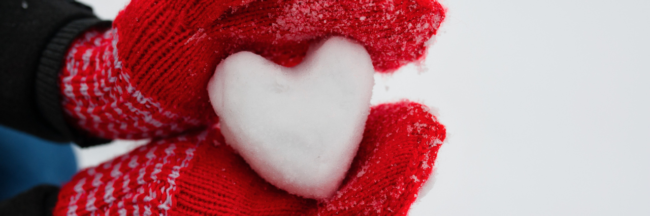 person wearing red gloves and holding a snowball shaped as a heart