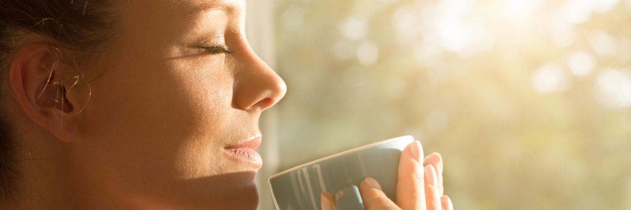 woman sipping her coffee and watching the sunrise while smiling