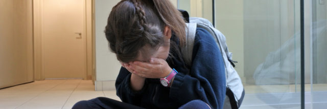 Girl wearing school uniform crying on the floor not wanting to go to school.