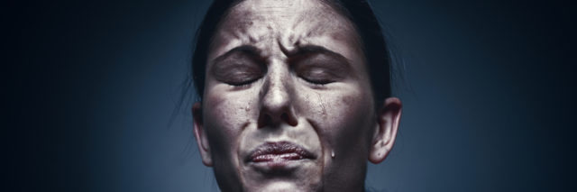 Close up portrait of a crying woman with bruised skin and black eyes at studio.