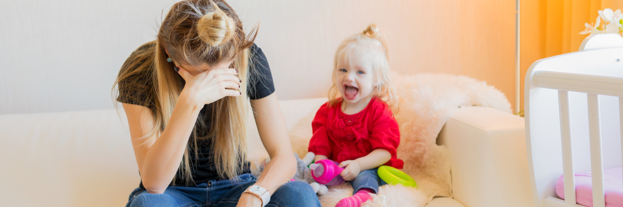 Being Diagnosed With Multiple Myeloma Gives Me a Mixture of Emotions A mom sitting with her head down and hand on her forehead while her little girl sits next to her.