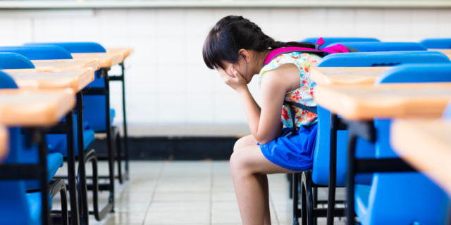 Girl alone in classroom covering her face with her hands