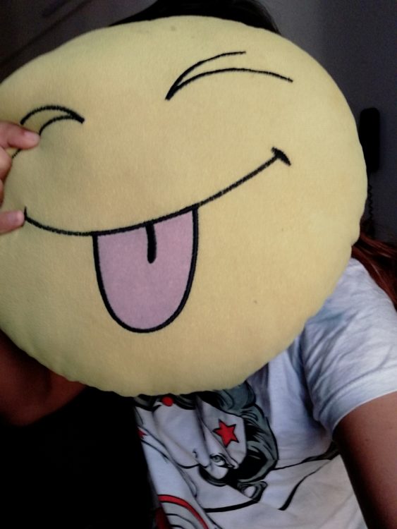 woman holding an emoji pillow in front of her face