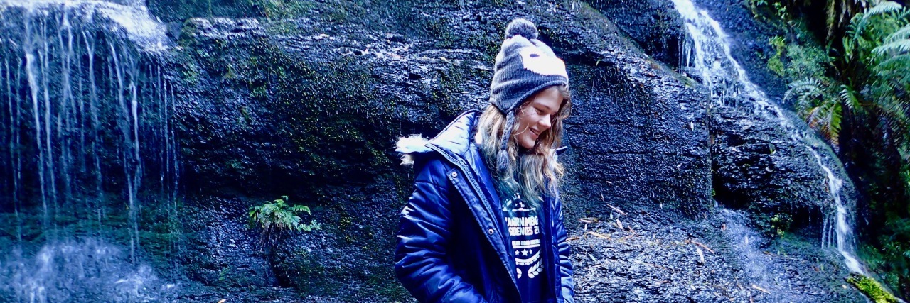 Why People With Fibromyalgia Shouldn't Compare Their Pain the author wearing a coat and hat and walking by a waterfall