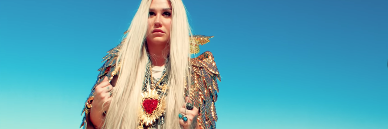 still screenshot of kesha in video for praying wearing bright clothes against blue sky