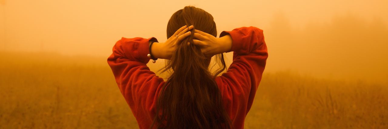 photo of woman facing away from camera with hands holding back of her head and orange mist in front of her.