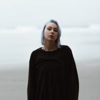 Woman with light blue hair standing outside and staring at camera